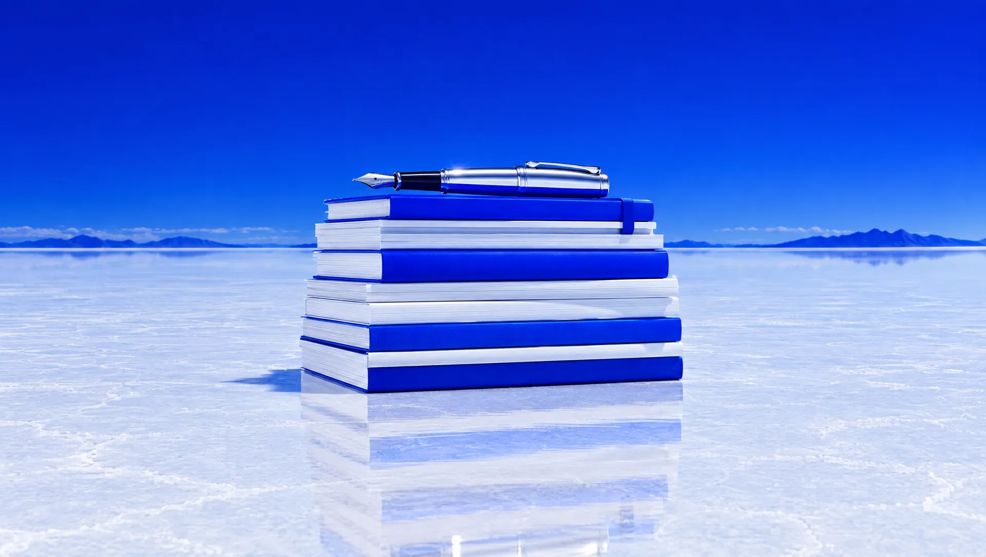A stack of white and blue editorial magazines with a chrome pen on a salt flat